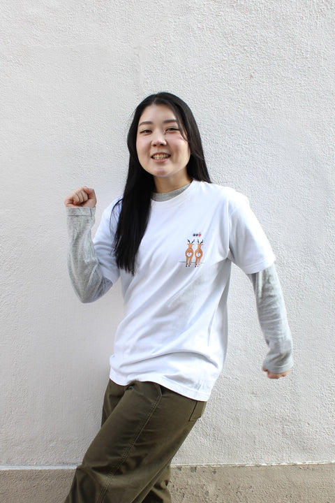 A model wearing a gray long-sleeve T-shirt layered with a white “Deer Walk” graphic T-shirt, styled casually with olive green pants against a simple wall background.