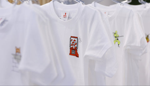 Row of white graphic T-shirts on hangers, featuring small chest art (gachapon, ninja) at ONE POINT.