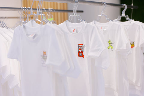 Row of white graphic T-shirts on hangers, featuring small chest art (gachapon, ninja) at ONE POINT.