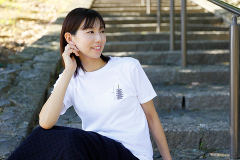 Model wearing a white tee with a small “Five-story Pagoda & Kaiju Monster” chest graphic, seated on stone steps.