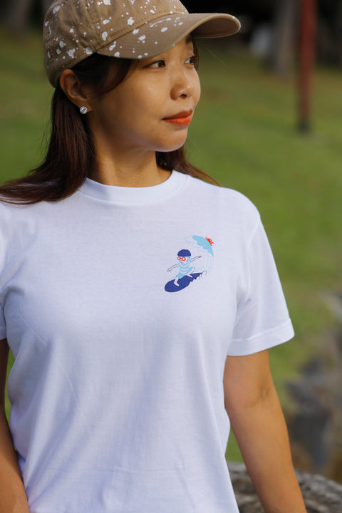 Woman wearing a white T-shirt named “Surfing”, featuring a small printed design of a person surfing on the chest.