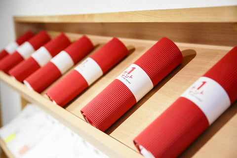 Rolled red T-shirt packaging displayed on a wooden shelf in store.