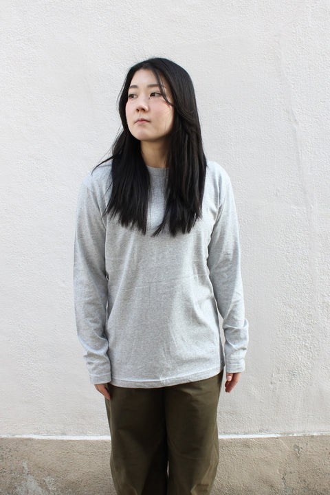 A person wearing a gray long-sleeved T-shirt, standing against a white wall