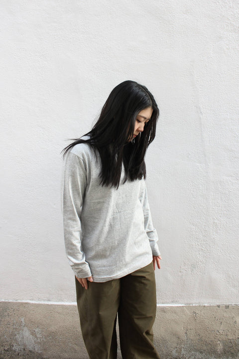A person wearing a gray long-sleeved T-shirt, standing against a white wall