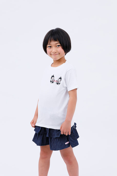 Front view of a smiling child wearing the white "Sumo Wrestler & Ayatori" T-shirt and a navy skirt, standing casually.