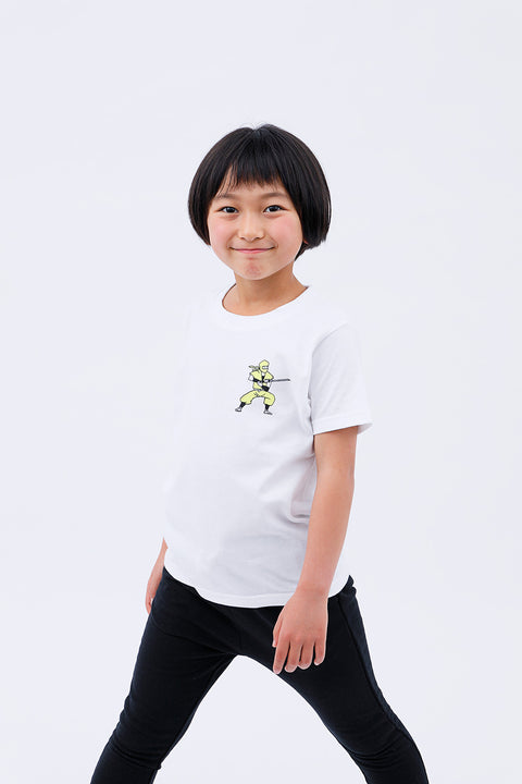 Front view of a smiling child wearing the white "Ninja" T-shirt and black pants, standing with one knee slightly bent.