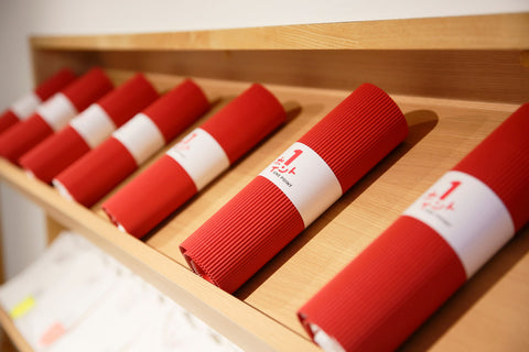 Rolled red T-shirt packaging displayed on a wooden shelf in store.